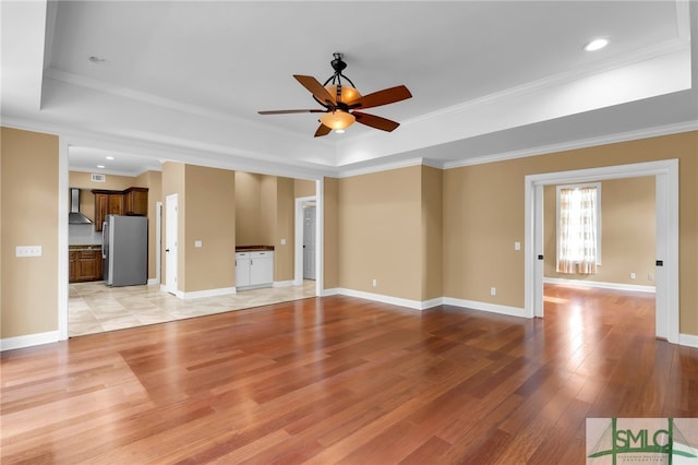 unfurnished living room with light wood-type flooring, crown molding, ceiling fan, and a raised ceiling