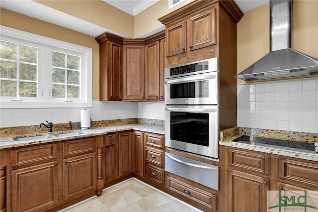 kitchen with light stone counters, sink, wall chimney exhaust hood, backsplash, and double oven