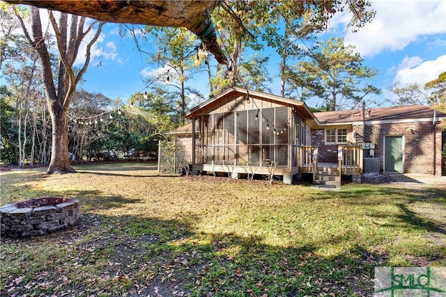 exterior space featuring a fire pit, a lawn, a sunroom, and a deck