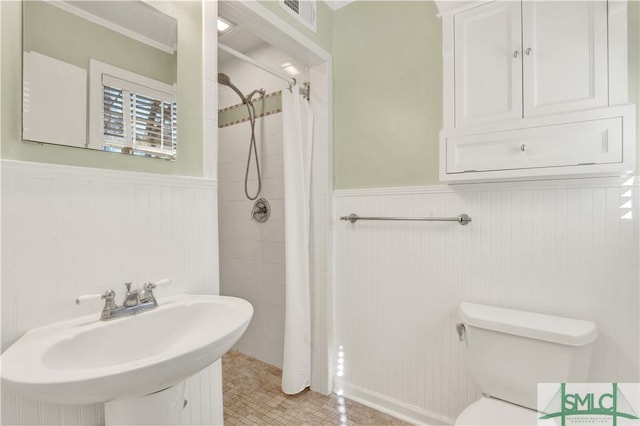 bathroom with a wainscoted wall, visible vents, a tile shower, and a sink