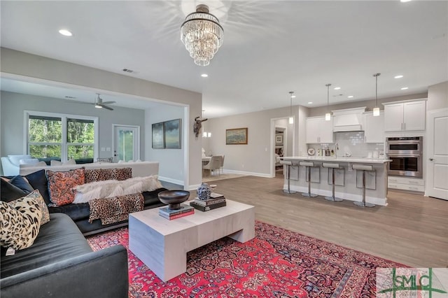 living room with sink, ceiling fan with notable chandelier, and light wood-type flooring