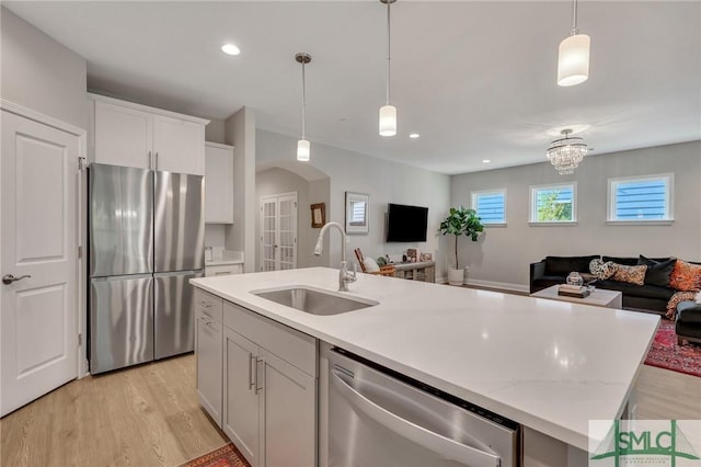 kitchen with decorative light fixtures, sink, white cabinets, a kitchen island with sink, and stainless steel appliances