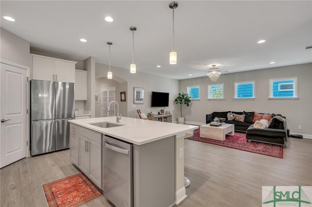 kitchen with sink, a kitchen island with sink, white cabinetry, stainless steel appliances, and decorative light fixtures