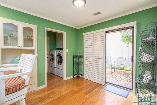 clothes washing area with cabinets, light wood-type flooring, crown molding, and washing machine and clothes dryer