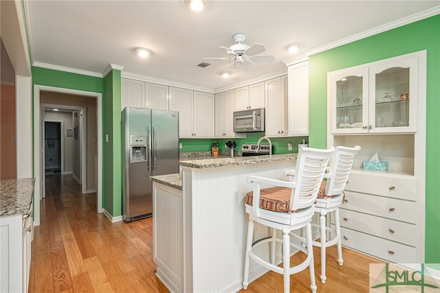 kitchen with white cabinetry, stainless steel appliances, crown molding, ceiling fan, and light hardwood / wood-style flooring