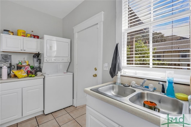 kitchen featuring stacked washing maching and dryer, sink, light tile patterned floors, and white cabinets