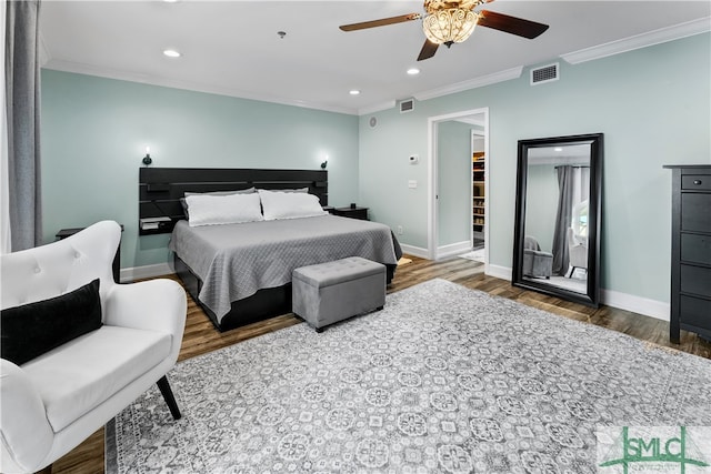 bedroom with crown molding, hardwood / wood-style floors, ceiling fan, and a walk in closet