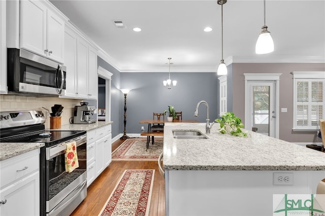 kitchen with stainless steel appliances, pendant lighting, sink, and a center island with sink