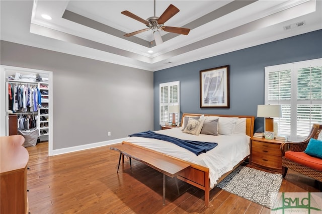 bedroom featuring ornamental molding, a spacious closet, light hardwood / wood-style flooring, and a tray ceiling