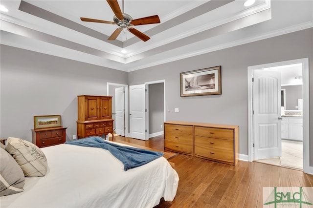 bedroom with a tray ceiling, ornamental molding, ceiling fan, light hardwood / wood-style floors, and ensuite bath