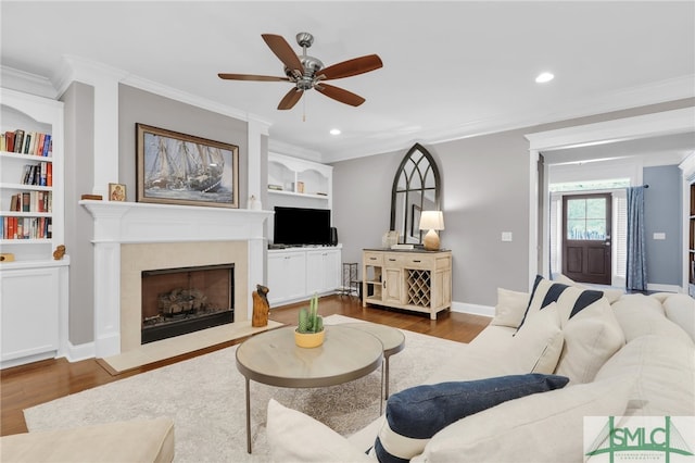 living room featuring ornamental molding, built in features, hardwood / wood-style flooring, ceiling fan, and a tiled fireplace