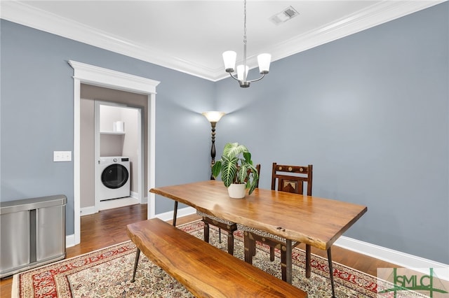 dining space featuring washer / clothes dryer, ornamental molding, dark wood-type flooring, and an inviting chandelier