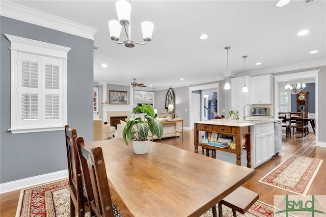 dining space with crown molding, ceiling fan with notable chandelier, sink, and light wood-type flooring