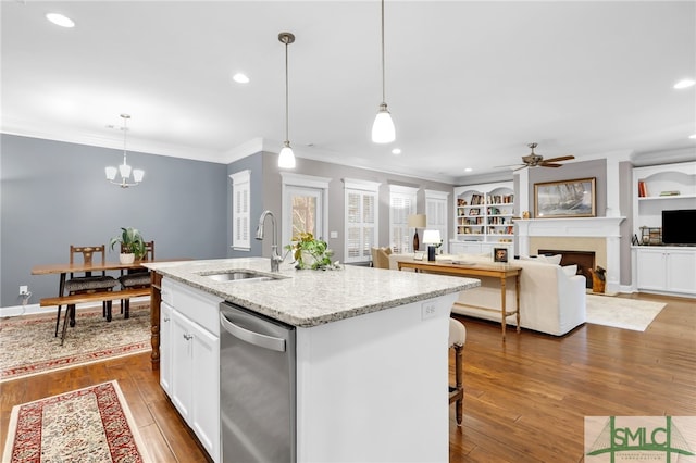 kitchen with a kitchen island with sink, sink, light stone counters, and hanging light fixtures