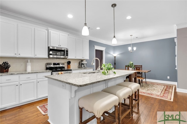 kitchen featuring stainless steel appliances, sink, decorative light fixtures, and a kitchen island with sink