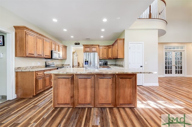 kitchen featuring light stone countertops, an island with sink, appliances with stainless steel finishes, and dark wood-type flooring