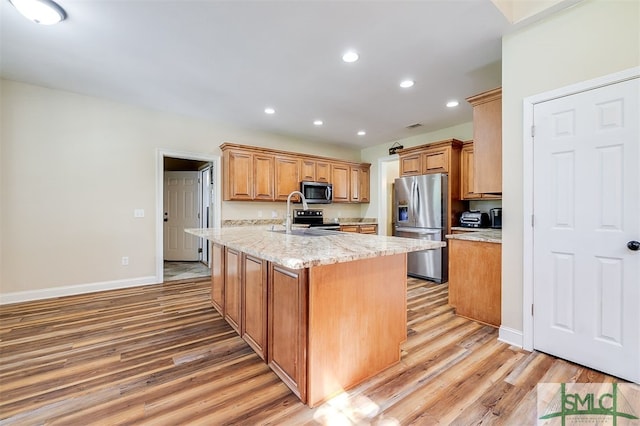 kitchen featuring light hardwood / wood-style floors, an island with sink, light stone countertops, stainless steel appliances, and sink