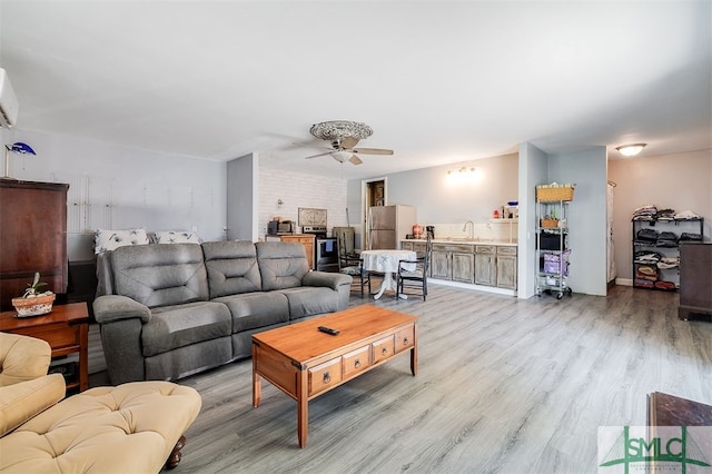 living room with a wall mounted AC, light hardwood / wood-style floors, ceiling fan, and sink