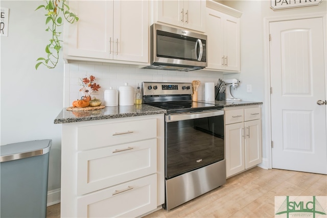 kitchen with appliances with stainless steel finishes, dark stone countertops, white cabinetry, backsplash, and light wood-type flooring