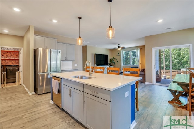 kitchen featuring appliances with stainless steel finishes, light hardwood / wood-style floors, ceiling fan, a center island with sink, and sink