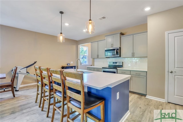 kitchen featuring pendant lighting, gray cabinets, stainless steel appliances, light wood-type flooring, and sink