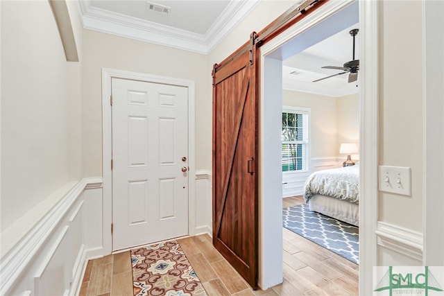 entryway featuring ornamental molding, light wood-type flooring, ceiling fan, and a barn door