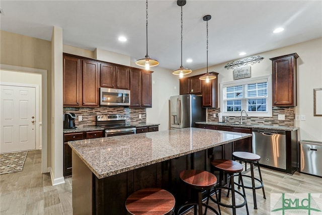 kitchen with light stone counters, a kitchen island, decorative light fixtures, stainless steel appliances, and light wood-type flooring