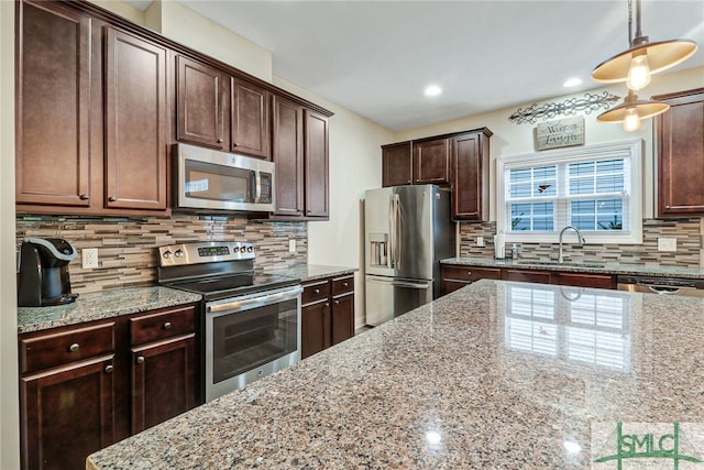 kitchen featuring tasteful backsplash, light stone countertops, stainless steel appliances, decorative light fixtures, and sink