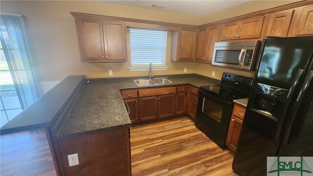 kitchen with light wood-type flooring, black appliances, sink, and kitchen peninsula