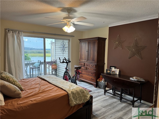 bedroom featuring light wood-type flooring, a textured ceiling, access to outside, ceiling fan, and a water view