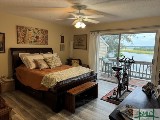 bedroom featuring access to exterior, hardwood / wood-style floors, a textured ceiling, and a water view