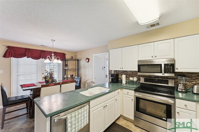 kitchen with sink, kitchen peninsula, white cabinetry, appliances with stainless steel finishes, and a notable chandelier