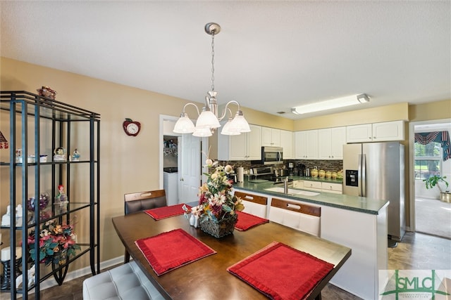 kitchen featuring stainless steel appliances, sink, white cabinetry, an inviting chandelier, and backsplash