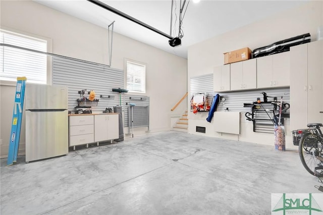 garage featuring a garage door opener, a workshop area, and stainless steel refrigerator