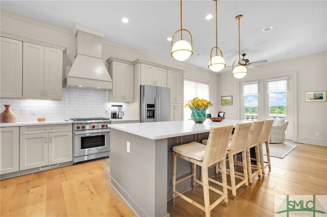 kitchen with hanging light fixtures, a kitchen bar, a kitchen island, custom range hood, and appliances with stainless steel finishes