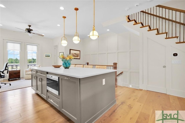 kitchen featuring ceiling fan, a center island, pendant lighting, light hardwood / wood-style floors, and gray cabinets