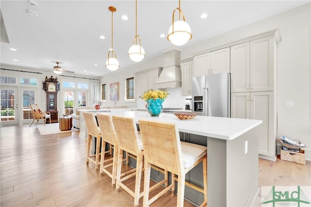 kitchen with a kitchen bar, high quality fridge, custom range hood, ceiling fan, and a spacious island