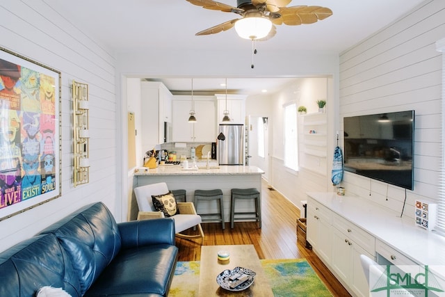 living room with ceiling fan, wooden walls, and light hardwood / wood-style flooring