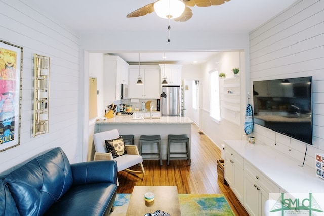 living room featuring light wood-type flooring, wood walls, sink, and ceiling fan