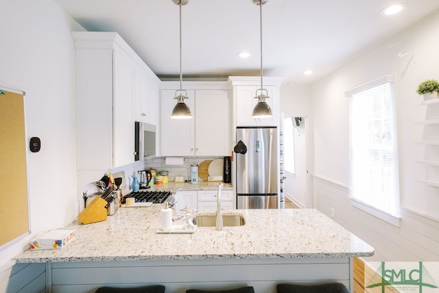 kitchen featuring a breakfast bar, white cabinets, appliances with stainless steel finishes, decorative light fixtures, and light stone countertops