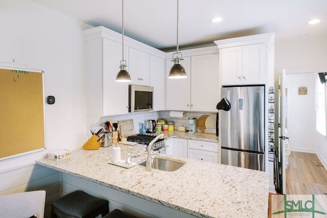 kitchen with white cabinetry, kitchen peninsula, hanging light fixtures, backsplash, and appliances with stainless steel finishes