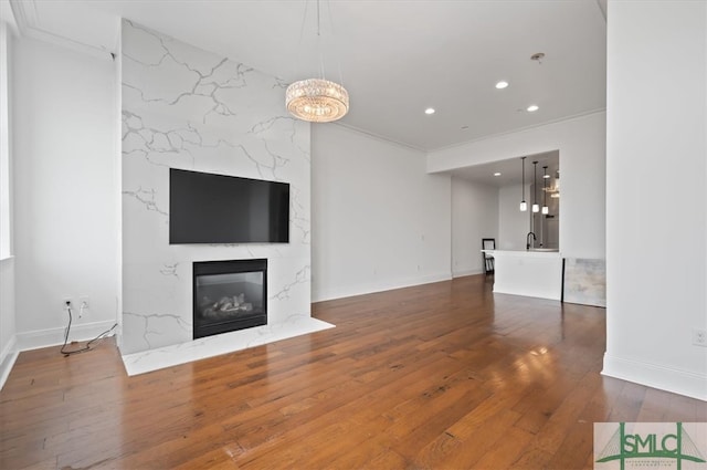 unfurnished living room with ornamental molding, a chandelier, a premium fireplace, and hardwood / wood-style flooring