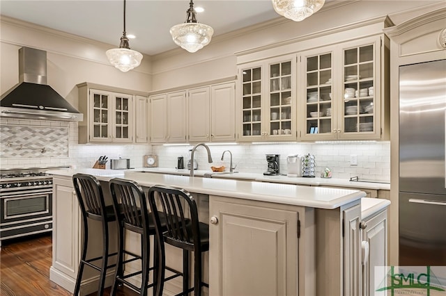 kitchen with premium appliances, a center island with sink, wall chimney exhaust hood, and decorative backsplash