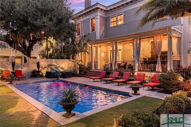 pool at dusk featuring a lawn and a patio