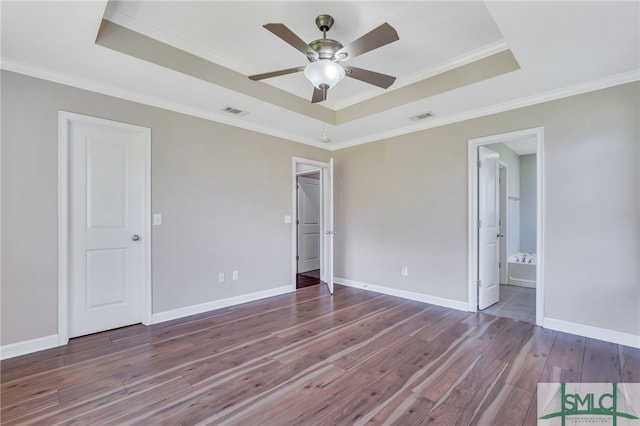 unfurnished bedroom featuring wood-type flooring, ensuite bath, and a raised ceiling