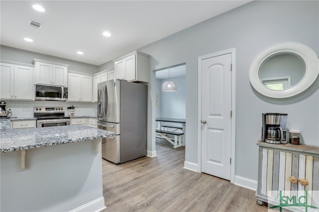 kitchen with tasteful backsplash, decorative light fixtures, white cabinetry, appliances with stainless steel finishes, and light hardwood / wood-style floors