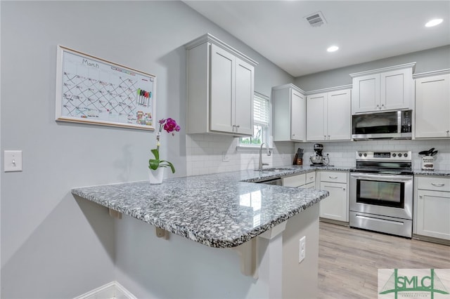 kitchen featuring light stone countertops, white cabinetry, kitchen peninsula, and appliances with stainless steel finishes