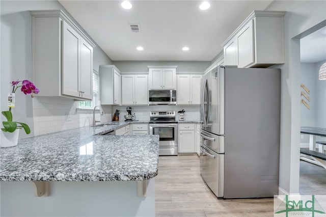 kitchen featuring white cabinetry, kitchen peninsula, appliances with stainless steel finishes, and light hardwood / wood-style floors