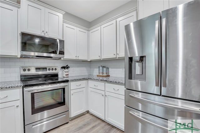 kitchen with light stone countertops, appliances with stainless steel finishes, light hardwood / wood-style floors, and white cabinetry