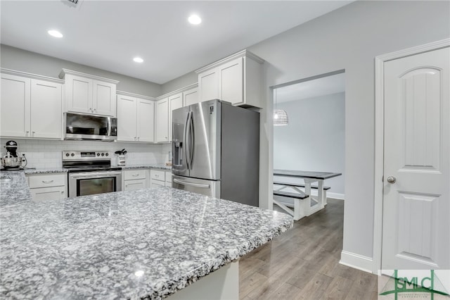 kitchen featuring white cabinets, appliances with stainless steel finishes, light stone countertops, light hardwood / wood-style floors, and decorative backsplash